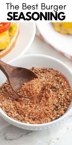 the best burger seasoning in a white bowl with a wooden spoon on top and another plate behind it