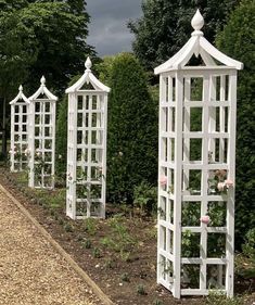 four white garden arbors lined up on the side of a road in front of trees