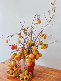 an arrangement of fruit is displayed in a vase on a wooden table with white walls