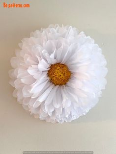 a white flower with yellow center sitting on top of a table next to a wall