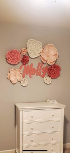 a white dresser sitting next to a wall with flowers on it