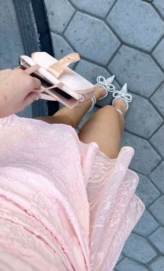 a woman in pink dress sitting on the ground with her legs crossed and holding a cell phone