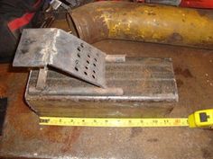 an old tool sits on top of a piece of metal with a measuring tape next to it