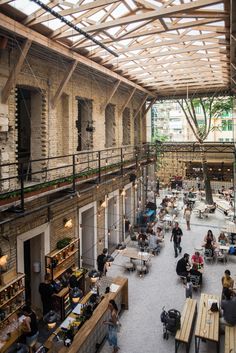 people are sitting at tables and eating in an open area with exposed ceilings, large windows, and wooden benches