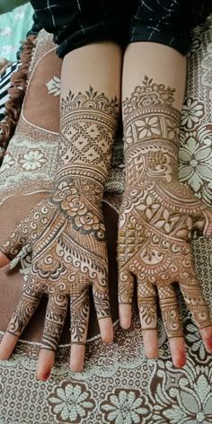 two hands with henna tattoos on them sitting on top of a bed next to each other