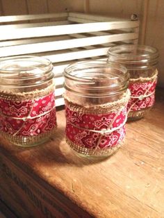 three mason jars are sitting on a wooden table with red and white fabric wrapped around them