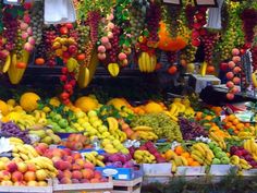 an outdoor fruit stand with lots of fruits and vegetables hanging from it's ceiling