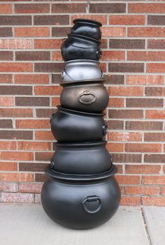 a stack of black vases sitting on top of a cement floor next to a brick wall