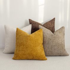 four different colored pillows sitting next to each other on a white carpeted floor in front of a window