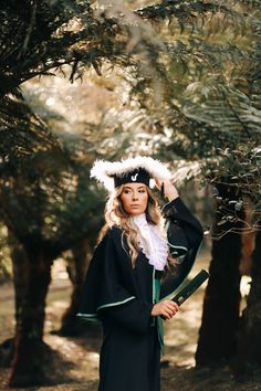 a woman wearing a black graduation gown and white fur stoler standing in front of trees