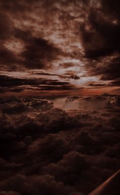 the view from an airplane looking down at clouds and sun in the sky with dark colors