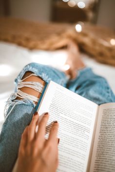 a woman laying on her side reading a book with ripped knees and nails attached to her leg