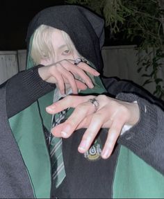 a person with blonde hair wearing a green and black hoodie holding their hand over his face