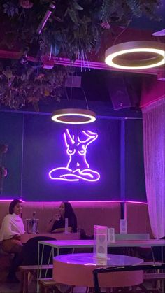 two people sitting at tables in front of a neon sign