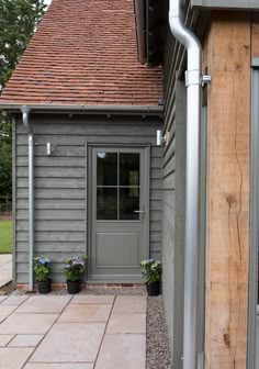 a small gray house with a red roof and brown shingles on the front door