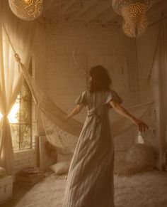 a woman in a white dress standing on a bed with a mosquito net hanging from the ceiling