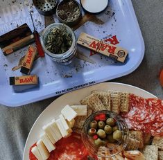 a plate with crackers, olives and cheese on it next to other snacks