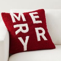 a red and white pillow that says merry sitting on a white couch with the words merry written across it