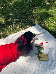 a woman laying on top of a white blanket next to a red rose and book