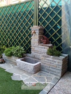 a stone fountain in the middle of a garden with green grass and plants around it