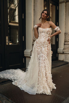 a woman in a wedding dress standing on the sidewalk with her hand on her hip