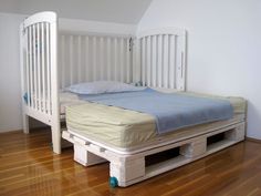 a white bed frame with two mattresses on top of it and a wooden floor