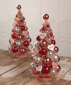 two small pink and silver christmas trees sitting on top of a wooden table next to each other