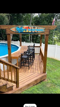 a wooden deck with chairs and a table next to a swimming pool that has a surfboard on it