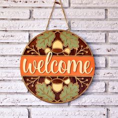 a welcome sign hanging from the side of a brick wall with acorns and leaves