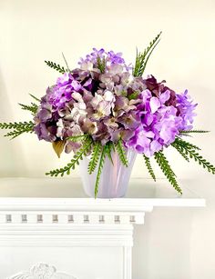 purple and white flowers in a vase on a mantle