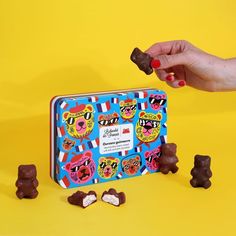 a person is holding some chocolate candies in front of the candy tin with bears on it