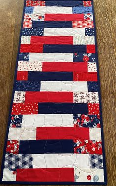 a red, white and blue patchwork quilt on a wooden table with a black border