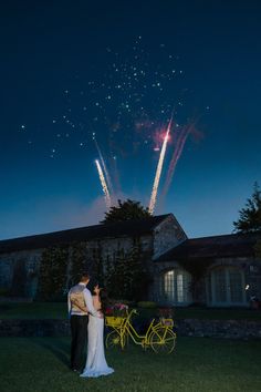 a bride and groom standing in front of a firework display