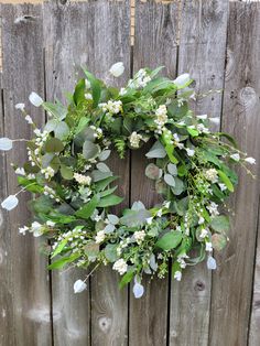 a wreath with white flowers and greenery hangs on a wooden fence in front of a wood paneled wall