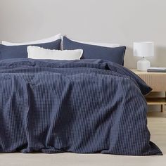 a bed with blue sheets and pillows on top of it, next to a night stand