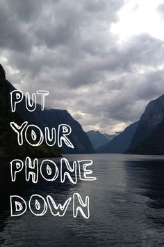 the words put your phone down are written in white ink on a lake with mountains and clouds