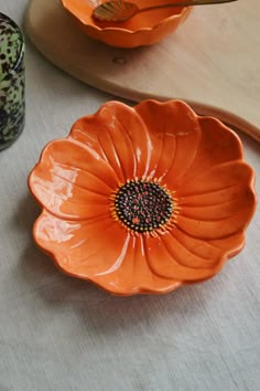 an orange flower shaped bowl sitting on top of a table next to a wooden spoon