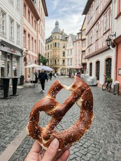 a person holding up a pretzel in the middle of a cobblestone street