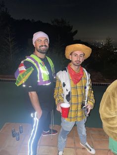 two men standing next to each other in front of a pool at night with lights on