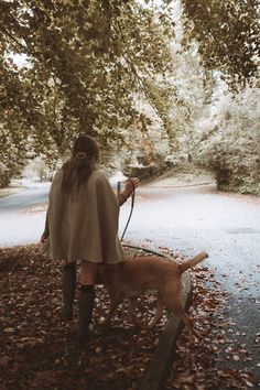 a woman is walking her dog through the leaves