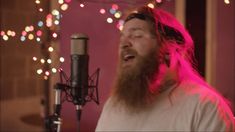 a bearded man singing into a microphone in front of a christmas tree with pink lights