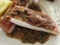 two pieces of meat on a white plate with peas and lemon wedges next to it