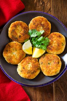 several crab cakes on a plate with lemon wedges and parsley