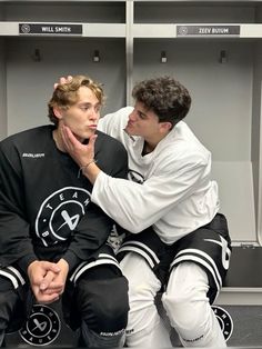 two young men sitting next to each other on a bench in front of lockers