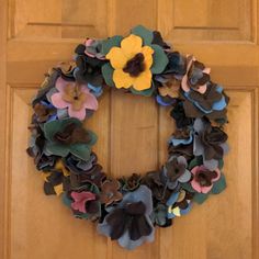 a wreath made out of paper flowers is hanging on the front door's wooden door