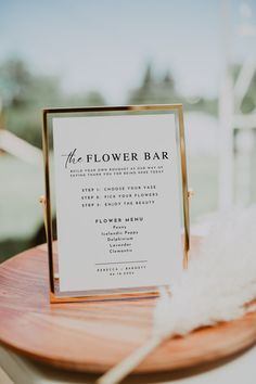 a flower bar sign sitting on top of a wooden table next to a white feather