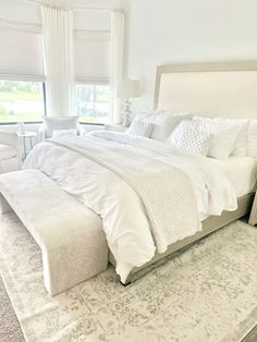 a large white bed sitting in a bedroom next to a window with curtains on the windowsill