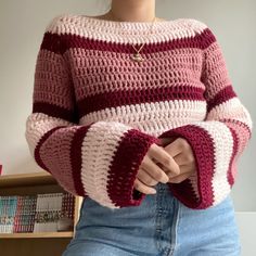 a woman wearing a pink and red sweater standing in front of a book shelf with her hands on her hips