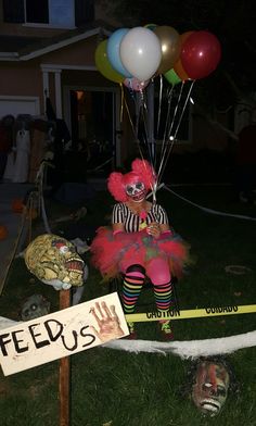 a creepy clown sitting on top of a barricade with balloons attached to it