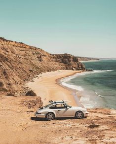 a white car parked on the side of a cliff near the ocean with surfboards on top